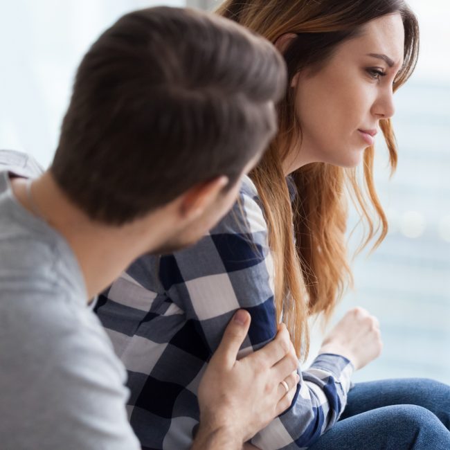 Loving husband comfort upset offended wife, caressing and hugging her from behind, caring man make peace and reconcile with lover, show support, couple in fight overcome family problems together